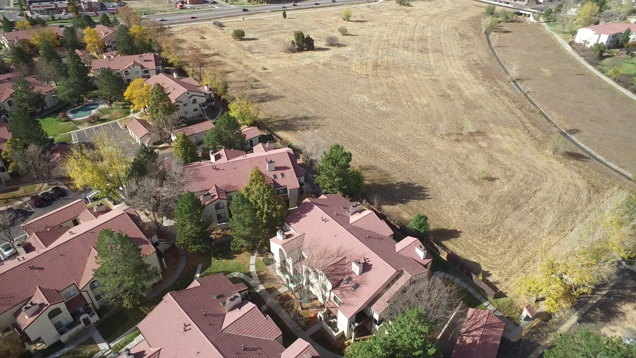 Aerial view in Hidden Lake, Colorado showing red-roofed homes, trees, driveways, and a dry open field to the right, with no recognizable people visible.