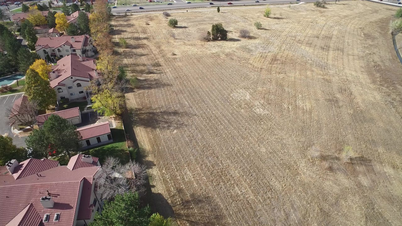Overhead view of dry field beside red-roofed homes and roads.