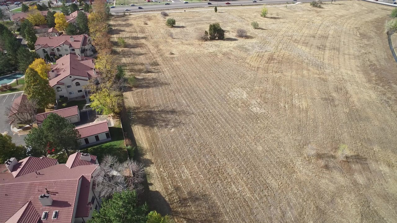 High drone view in Hidden Lake, Colorado with the field filling the center, homes and trees along the left side, a road at the top, and no visible people.