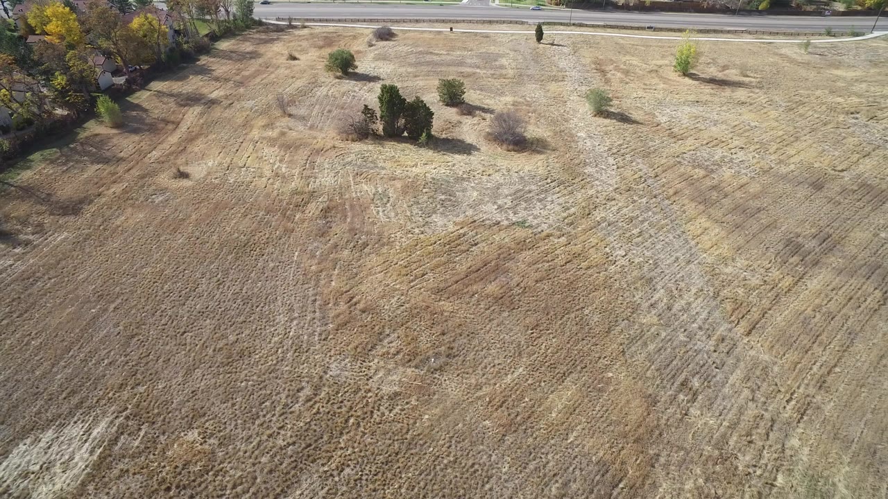 Aerial frame from Hidden Lake, Colorado showing dry tan ground, scattered trees, a road along the upper edge, and no visible people.