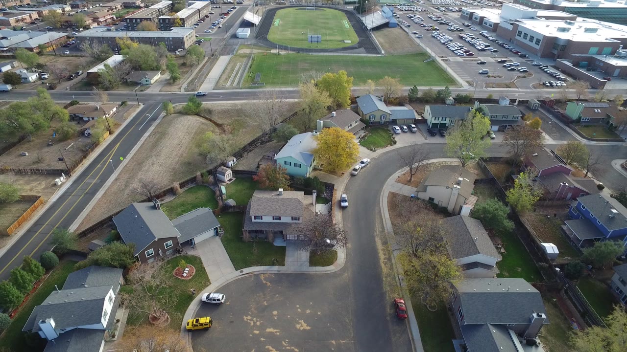 Aerial view of curved residential streets, houses, parked cars, and a nearby sports field.