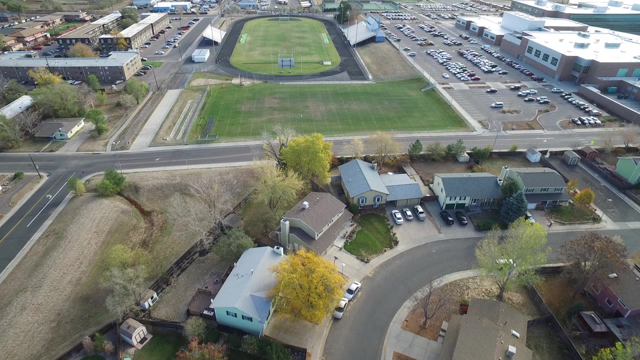 Drone view over suburban homes toward a green field and track.