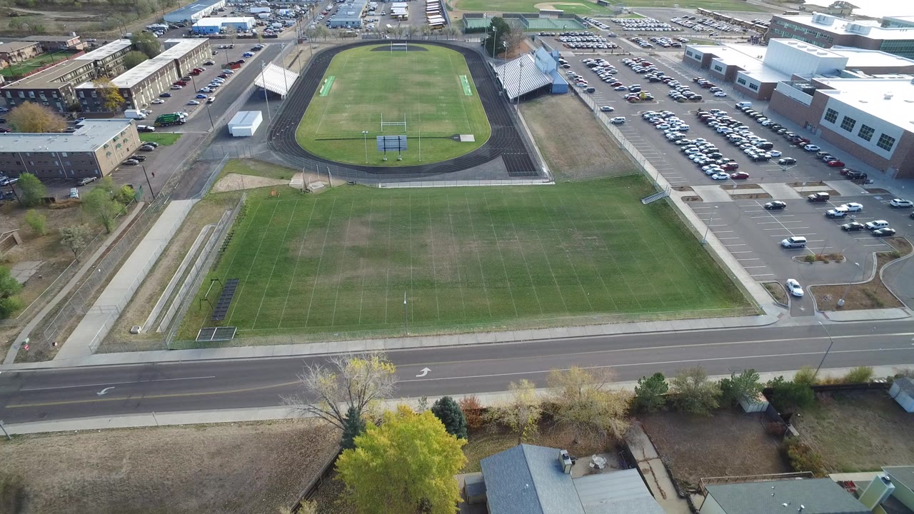 Aerial view of football field, track, parking lots, roads, and campus buildings.
