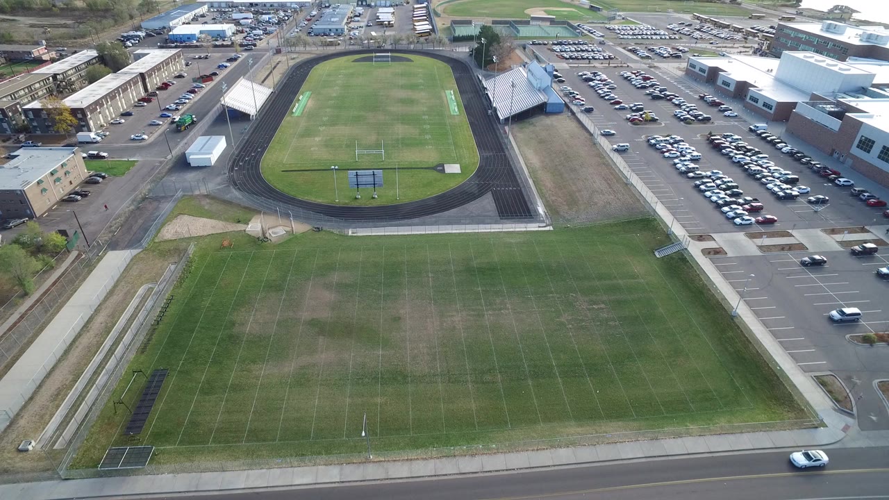 Aerial view of green fields, oval track, parking lots, and buildings.