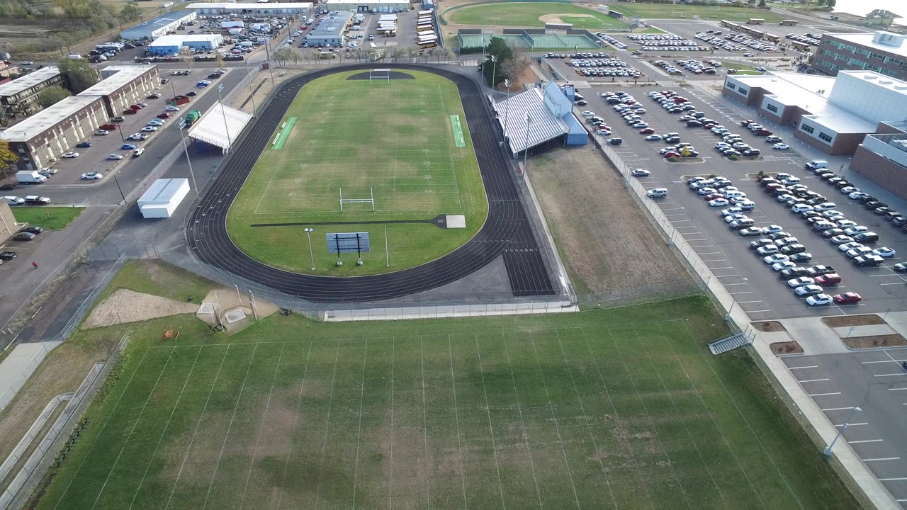 Aerial view of a green football field inside a running track beside parking lots.