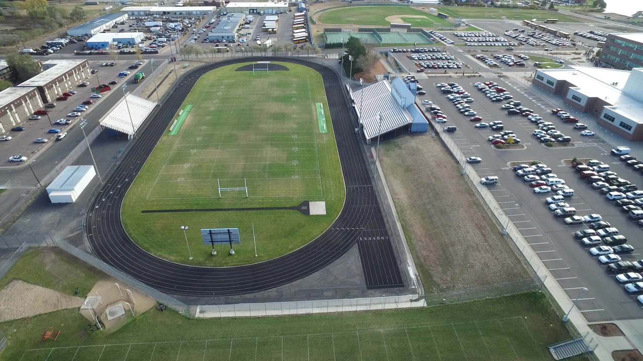 Aerial view of a football field inside a running track beside parking lots and bleachers.