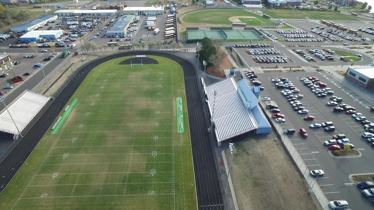 Aerial view of a football field, running track, bleachers, and parking lots.