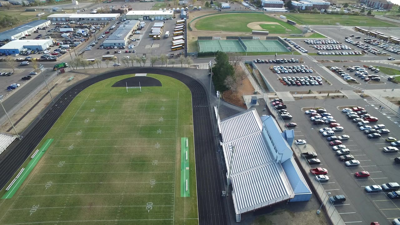 Aerial view of a football field, track, bleachers, parking lots, and tennis courts.