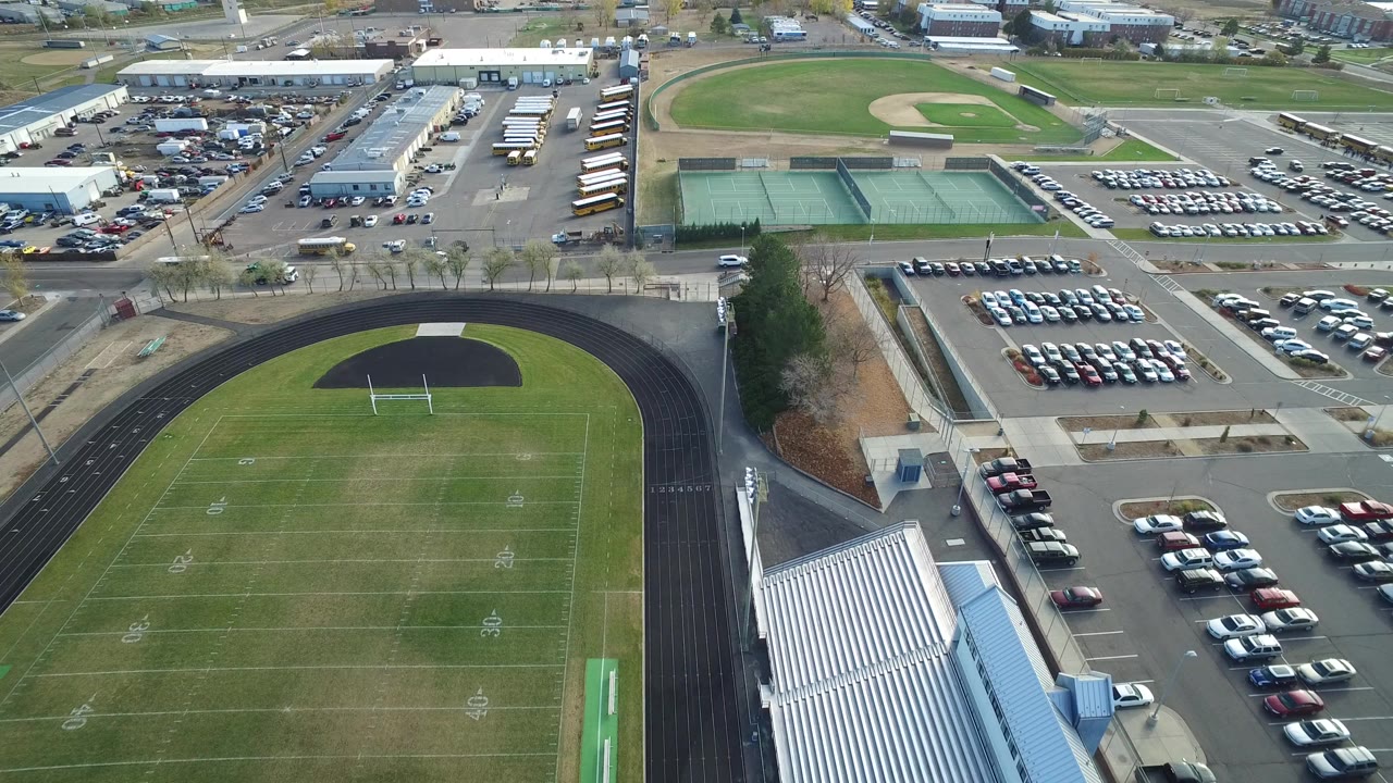 Aerial view of a football field, running track, bleachers, parking lots, tennis courts, and baseball field.