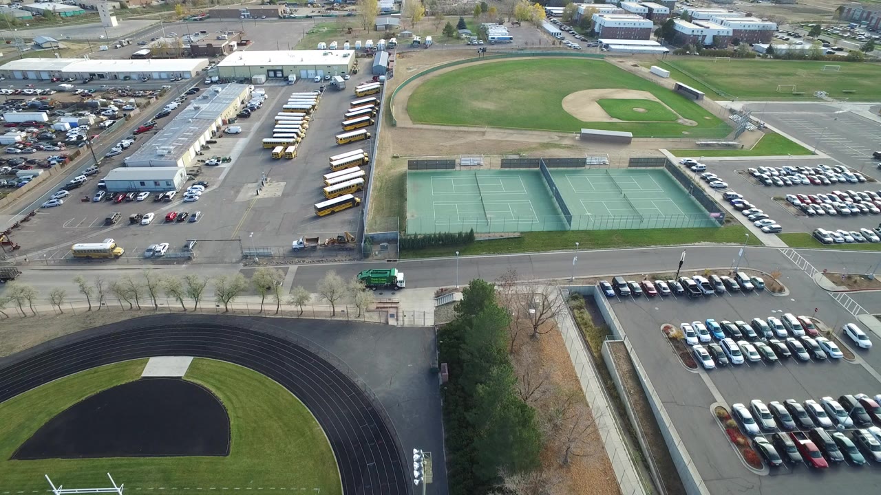 Aerial view of tennis courts, baseball field, parking lots, school buses, and a running track curve.