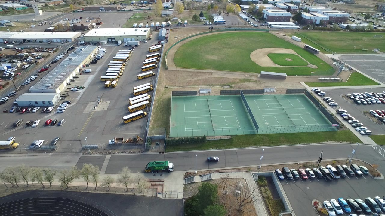 Aerial view of tennis courts, a baseball field, school buses, roads, and parking lots.