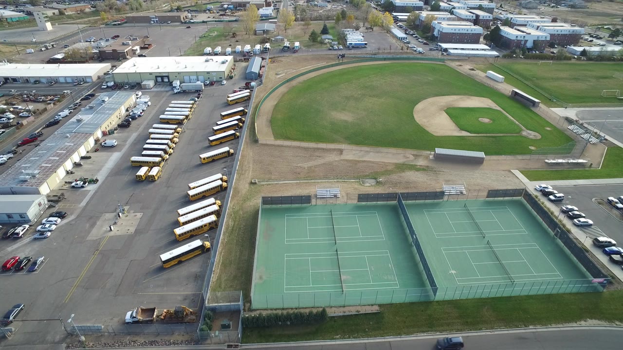 Aerial view of tennis courts, ball field, parking areas, buses, and low buildings.