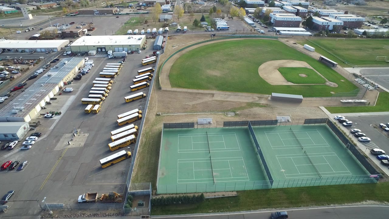 Second aerial frame over Hidden Lake, Colorado with the tennis courts centered lower in the view, the ball field above them, bus rows at left, parking at right, and no visible people.