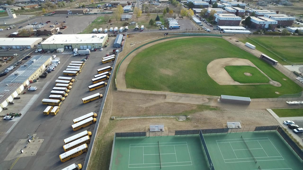 Aerial view of an empty baseball field beside tennis courts and parked school buses.