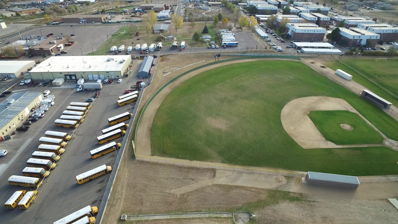 Aerial view of a baseball field beside rows of school buses and industrial buildings.
