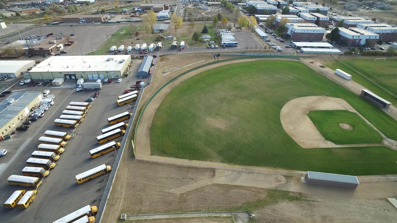 Hidden Lake, Colorado aerial view with the baseball diamond slightly right of center, the outfield filling the middle, rows of buses along the lower left edge, and no visible people.