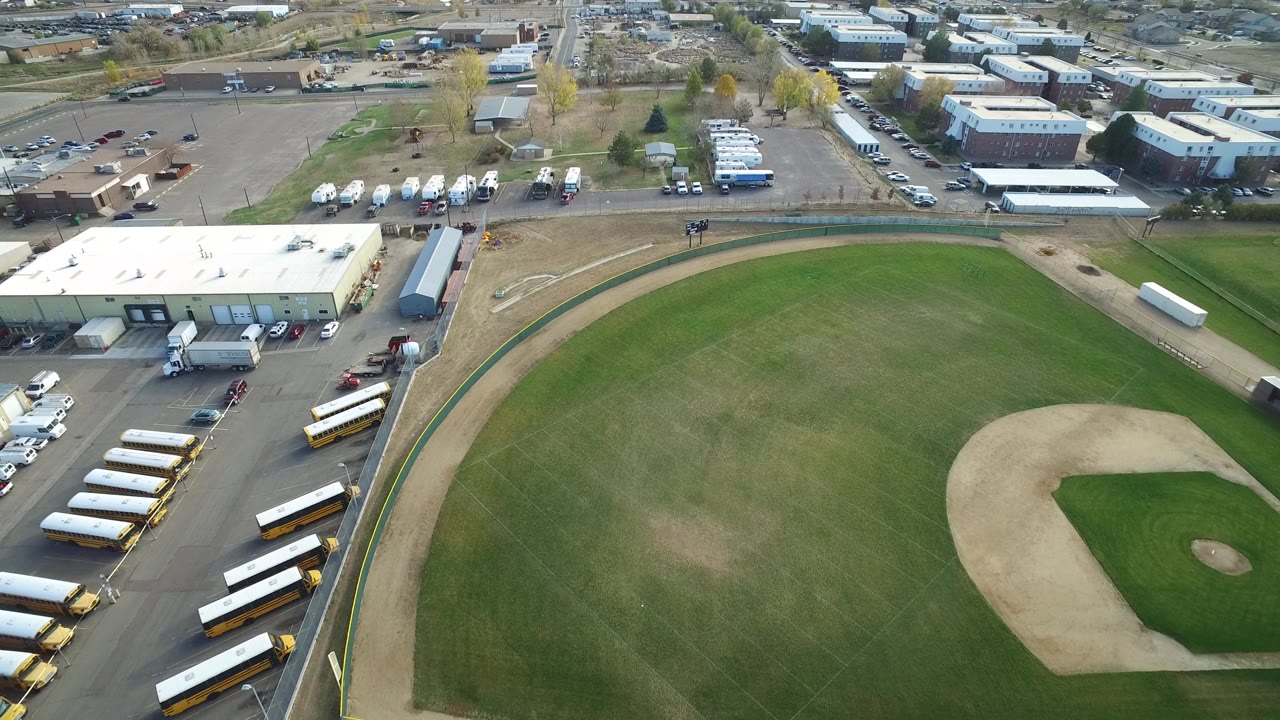 Aerial view in Hidden Lake, Colorado with the baseball outfield filling the lower frame, the infield to the right, and parked school buses and low buildings beyond it.