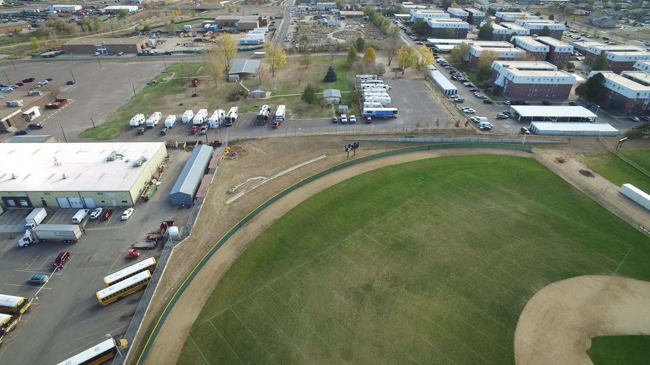 Aerial view of a green field beside warehouses, parking lots, buses, and service vehicles.