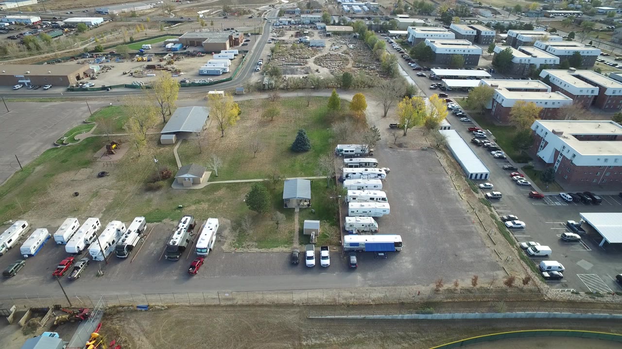 Aerial frame of Hidden Lake, Colorado showing an industrial park with white RVs at lower left, service buildings at right, parked cars, a drainage channel, and no visible people.
