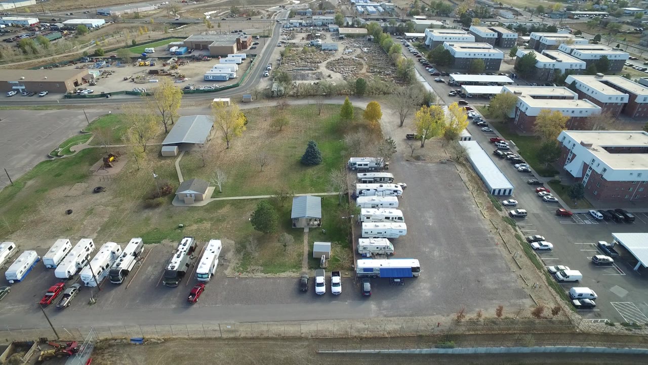 Drone-like view of an industrial park with a long white trailer, brick building, cars, and RV storage.