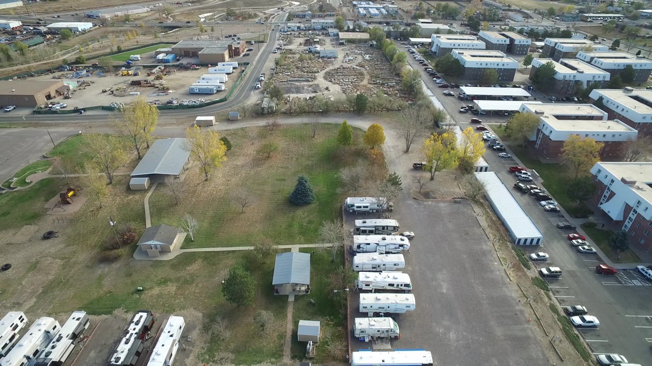 High aerial view in Hidden Lake, Colorado with the RV row lower in frame, open grass and trees at center, and roads plus low buildings beyond, with no discernible people.