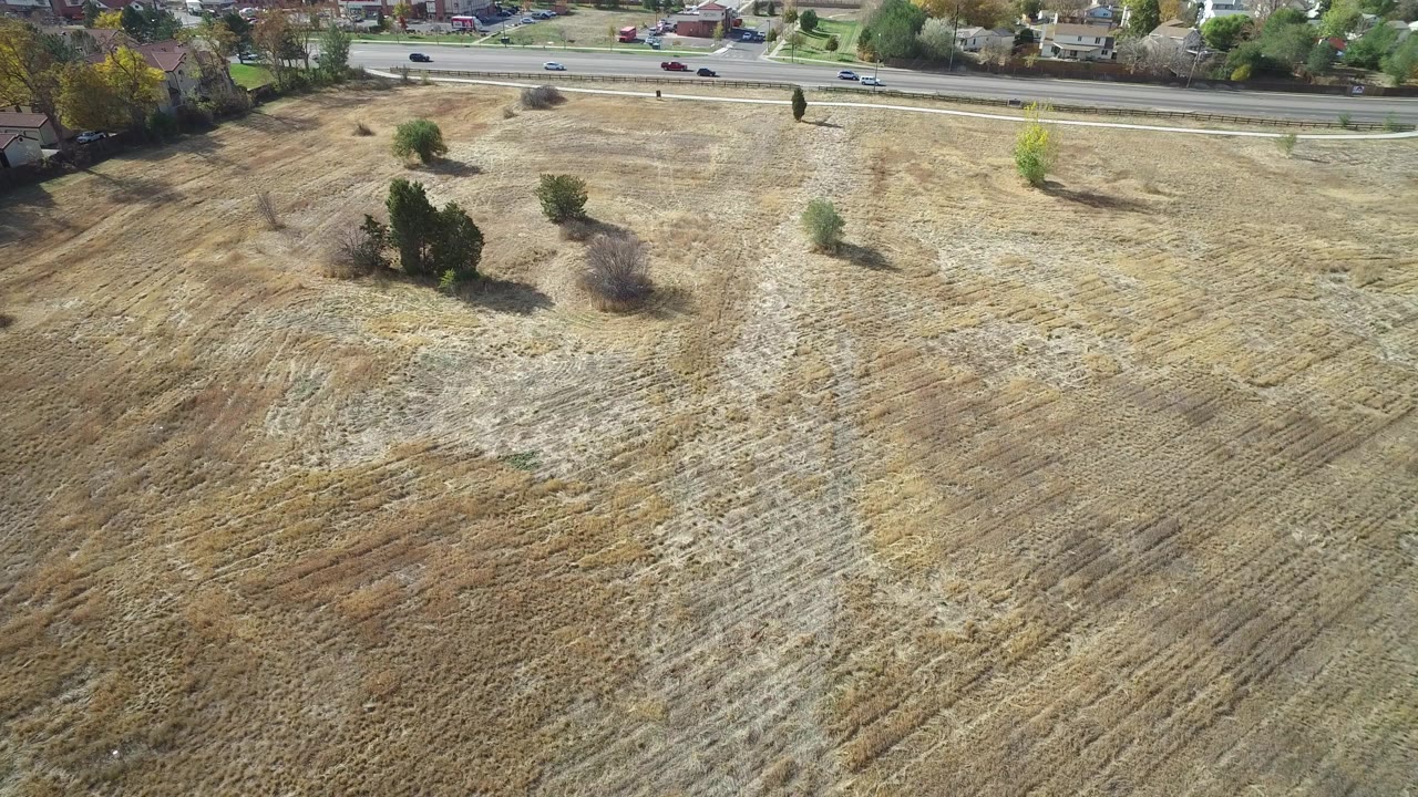Aerial view over a dry field beside a residential road with cars and houses.