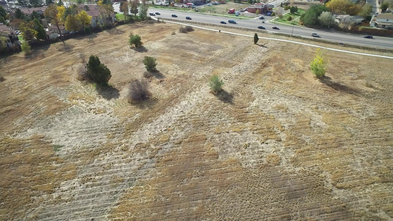 Aerial view of a dry field beside a road and suburban houses.