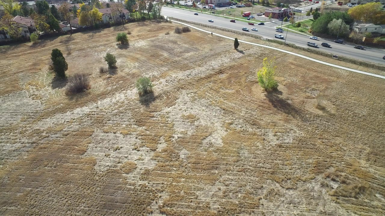 Aerial view of scrubby field below a busy road with cars.