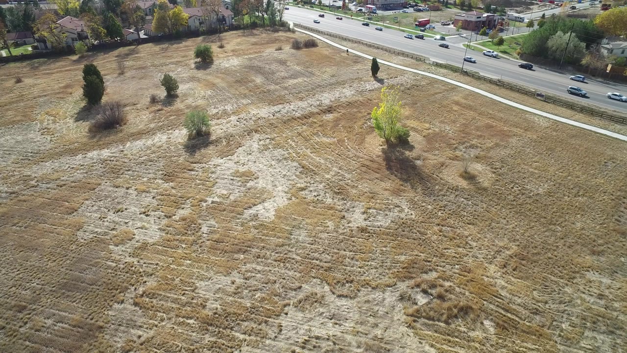 Aerial view of a dry field beside a road with cars and houses beyond.