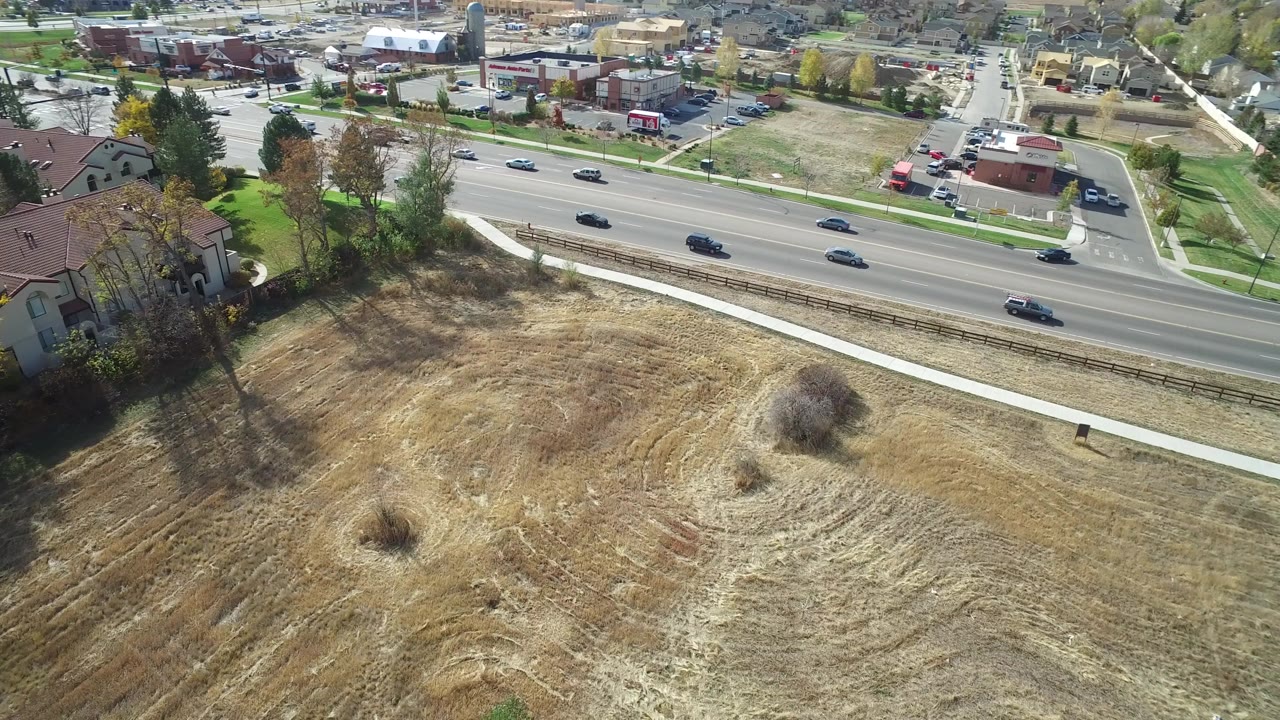 Aerial view of cars on a highway beside a dry field and suburban buildings.