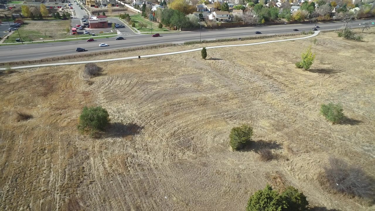 Elevated view of plowed land, trees, road traffic, and homes.