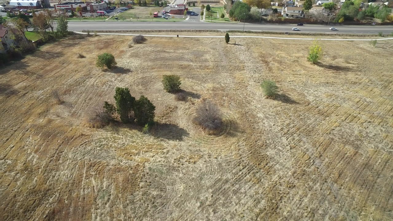 Aerial view in Hidden Lake, Colorado showing dry cleared grassland with scattered trees, a road and homes along the upper edge, and no visible people.