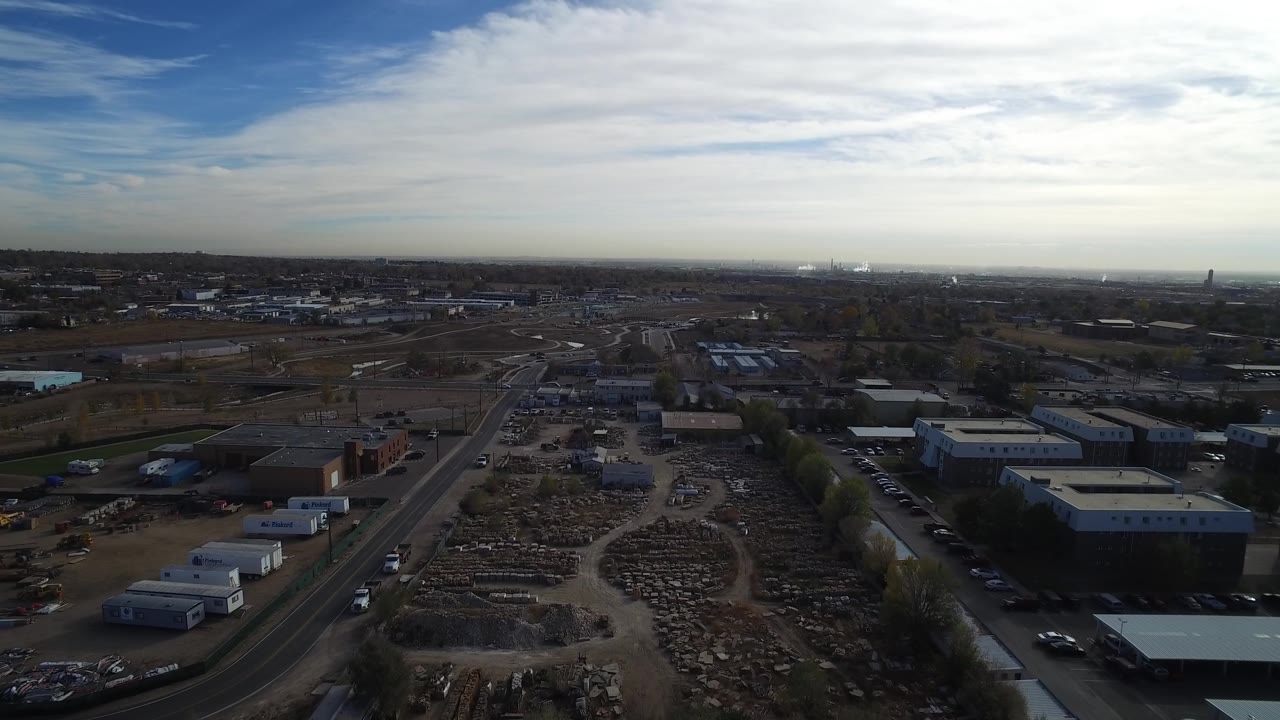 Aerial view of industrial buildings, roads, lots, and a wide cloudy sky.