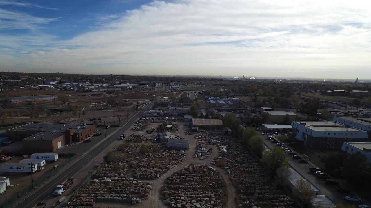 Aerial view in Hidden Lake, Colorado with open storage yards in the foreground, low industrial buildings to the right, a road corridor to the left, and no visible people.