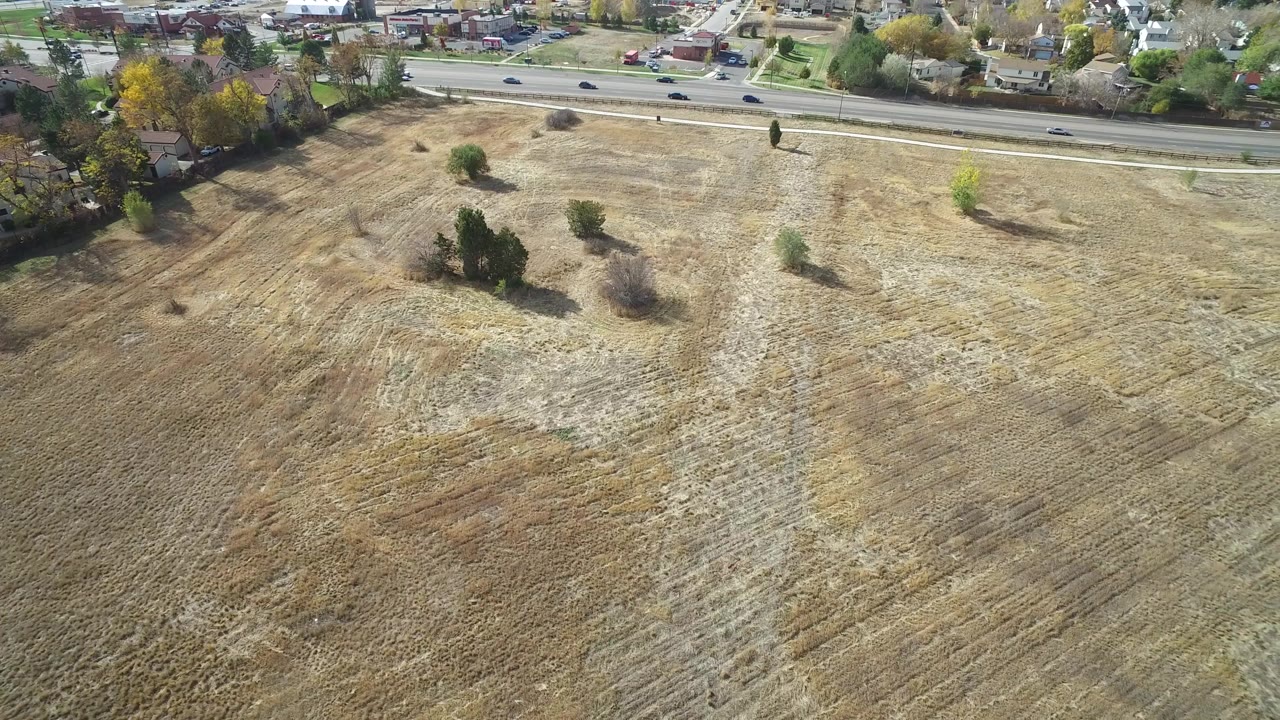 Aerial view in Hidden Lake, Colorado with the field dominating the foreground, small tree clusters near the road, several vehicles on the pavement, and no visible people.