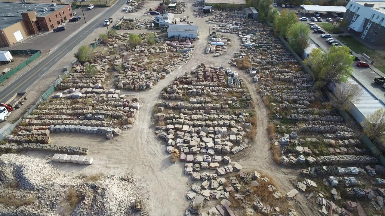 High aerial view in Hidden Lake, Colorado showing rows of rocks and scrap piles beside a paved road, with buildings and parked vehicles nearby and no visible people.