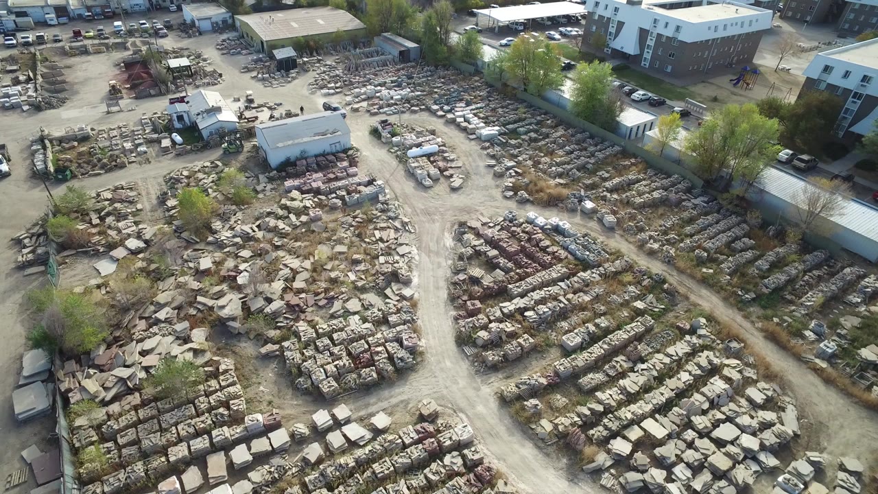 Aerial view over rows of stacked stone, dirt drives, parked cars, and buildings.