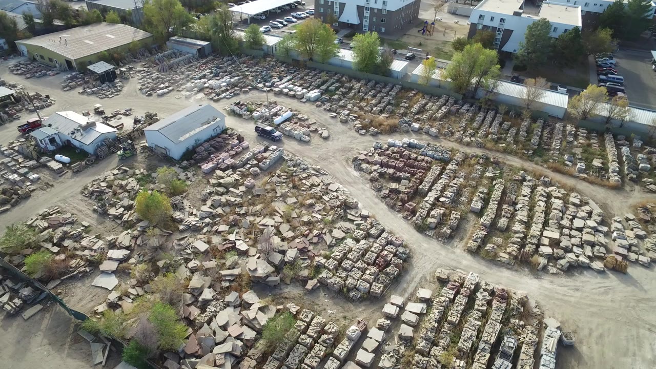 Aerial view of a waste yard with dirt roads, debris rows, buildings, and a white SUV.