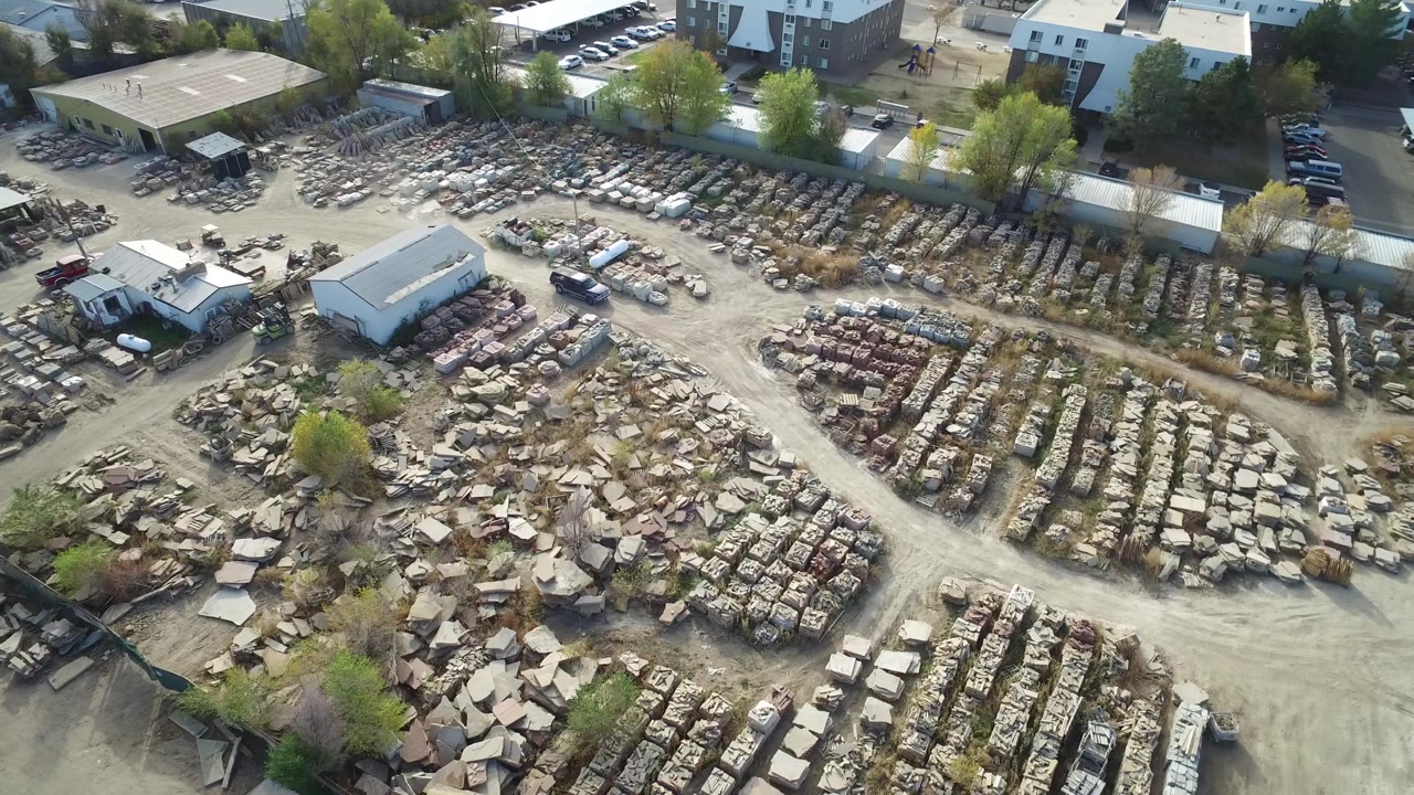 Aerial view in Hidden Lake, Colorado shows the white SUV farther along the central dirt lane, surrounded by rectangular scrap rows, rubble piles, service buildings, and no visible people.