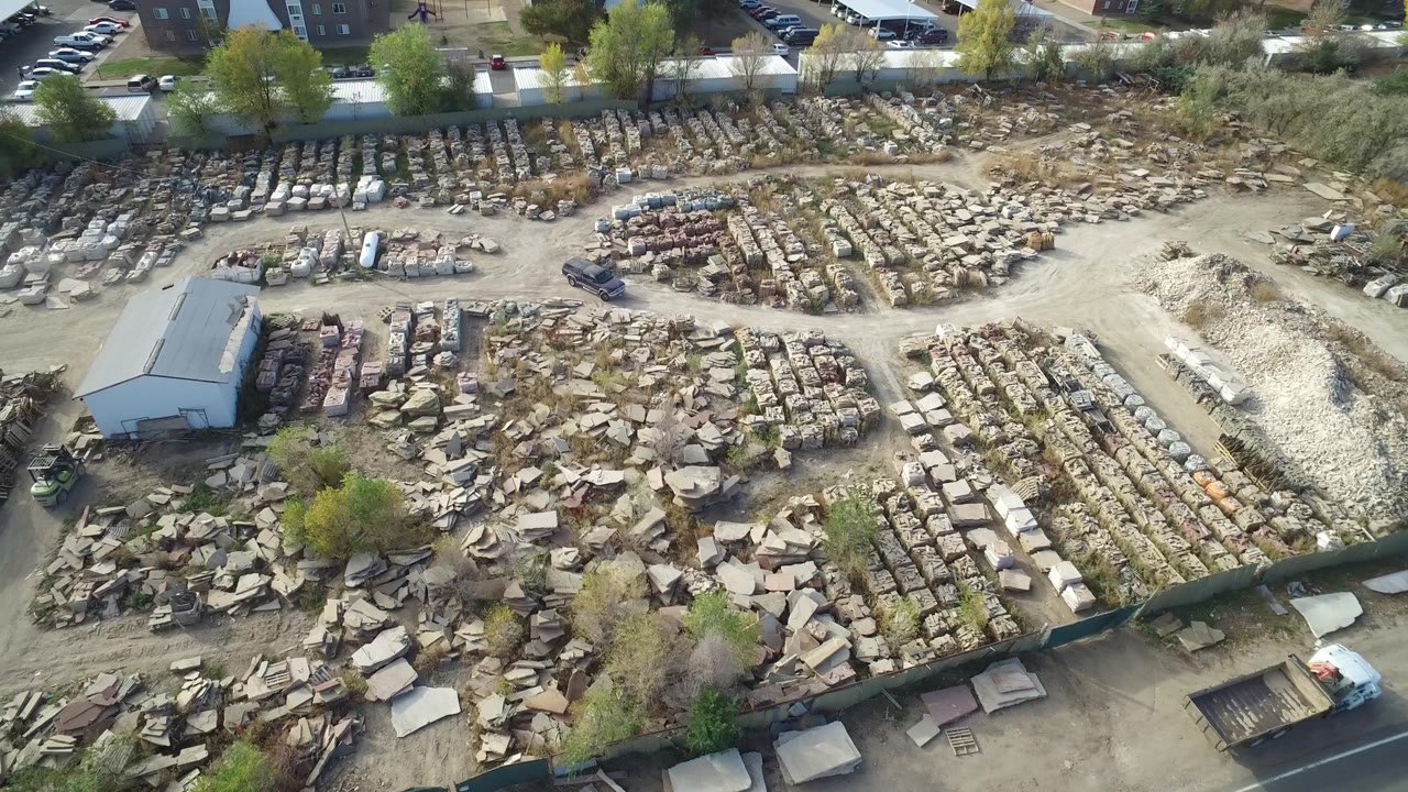 Aerial frame in Hidden Lake, Colorado showing a pale gravel mound, ordered rows of stone blocks, rough slab piles, a small shed, parked vehicles, and no visible people.