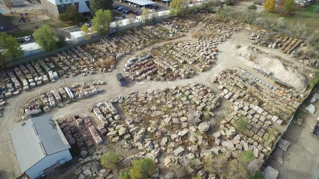 Overhead view of a stone yard with parked vehicles and nearby buildings.