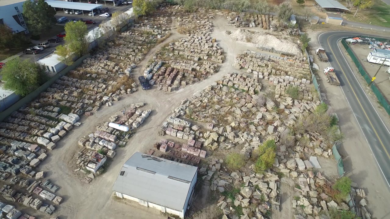 Aerial view of rock piles, a warehouse roof, and roadside trailers.