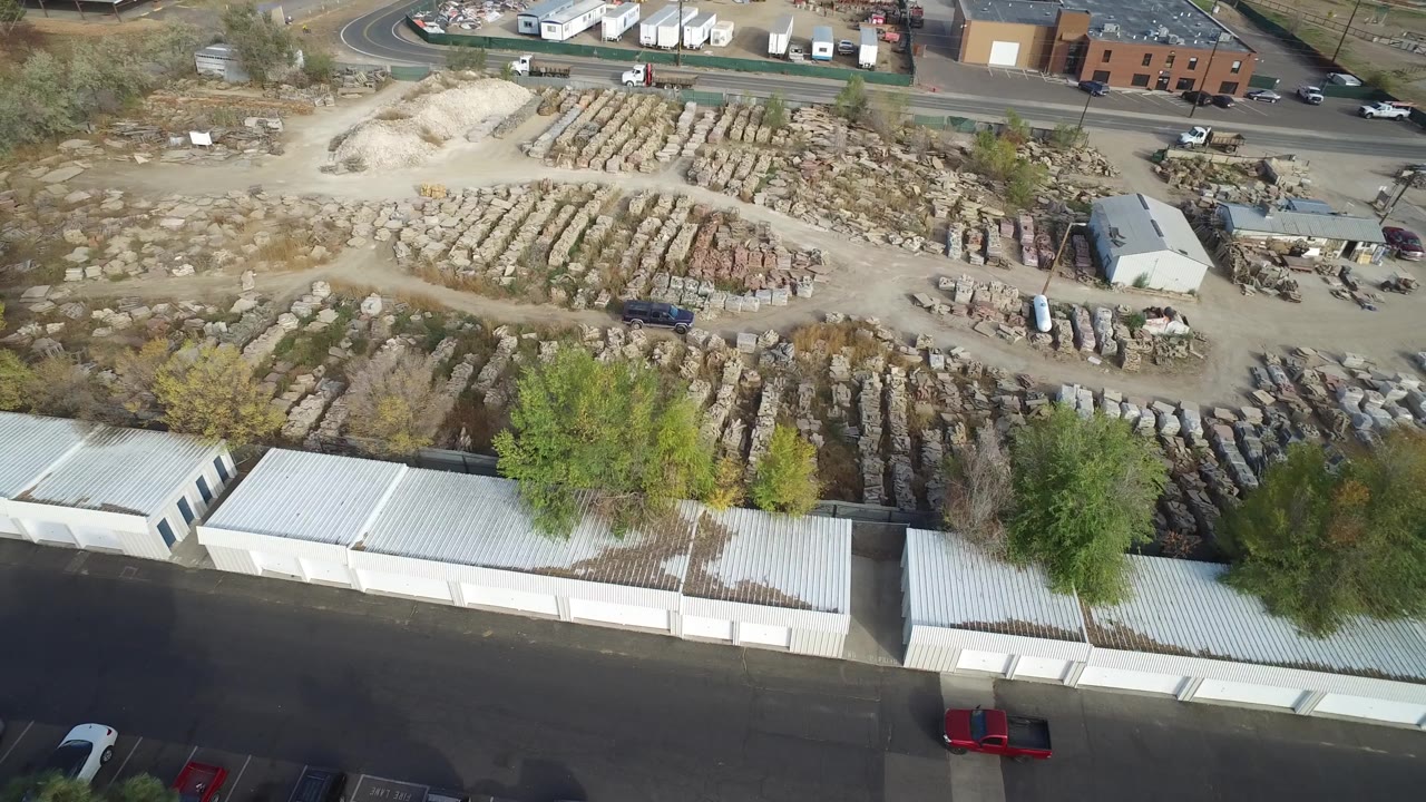Drone view over a dusty materials yard with storage units and vehicles near the road.