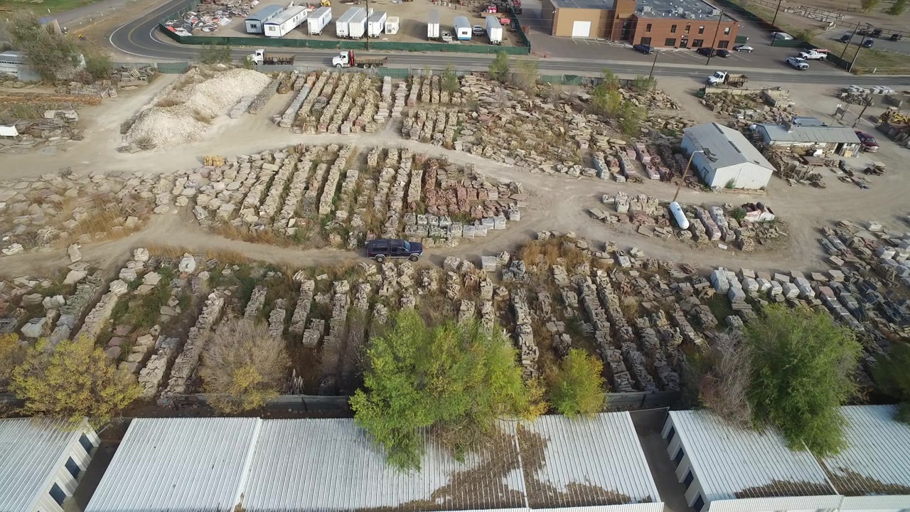 At 0:01, the Hidden Lake aerial view holds over organized stone rows, a pale gravel pile, a small shed, roadside vehicles, and foreground tree tops with no visible people.
