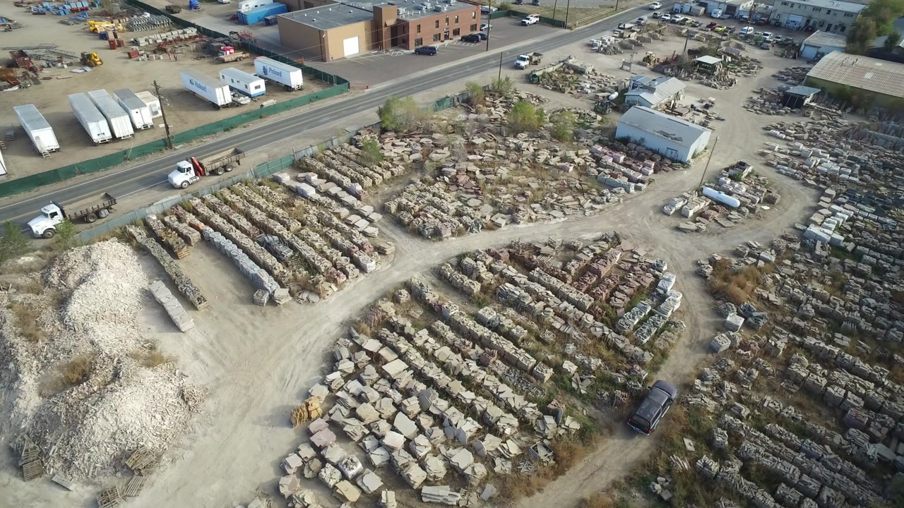 Aerial view of an industrial storage yard beside a road and warehouse buildings.