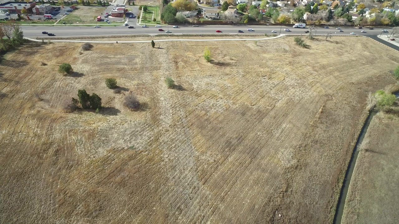 Aerial view of dry plowed field beside a multi-lane road and homes.