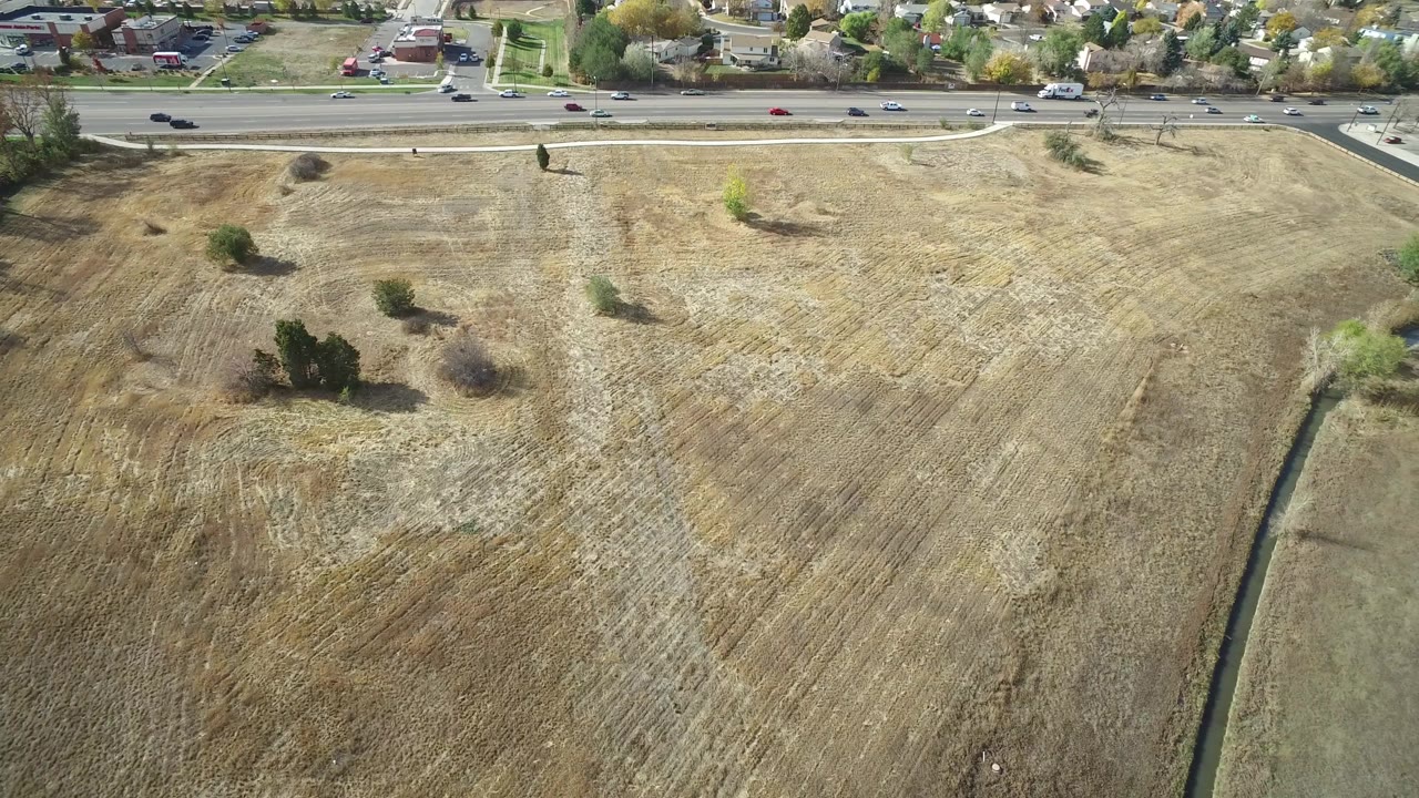Aerial view in Hidden Lake, Colorado with the field texture filling most of the frame, a straight road across the top, moving cars, background homes, and no visible people.
