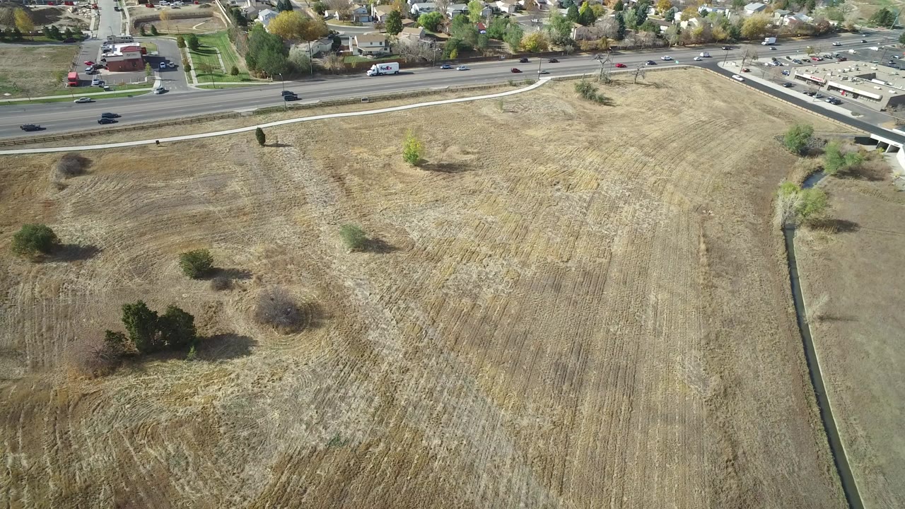 Aerial view over a dry field beside a road and neighborhood.