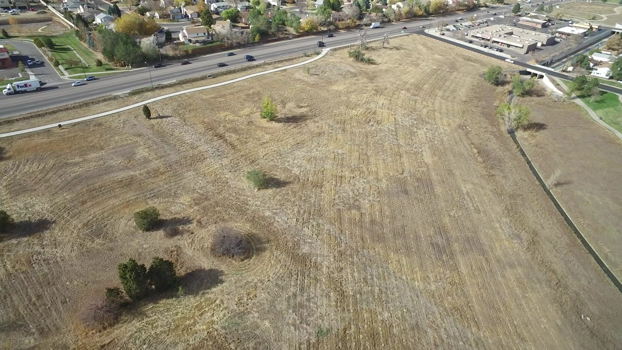 Aerial view of a cut grassy field beside a road and neighborhood.