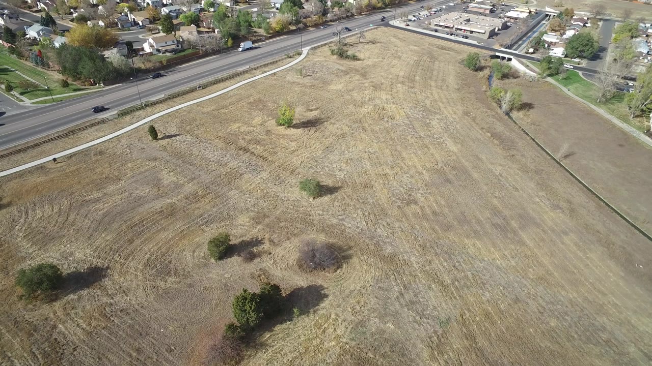 High aerial view of dry open field beside a road and neighborhood.